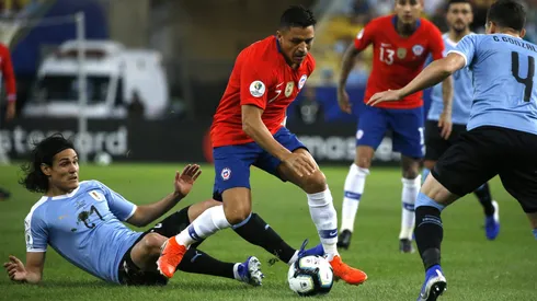 Alexis Sánchez avanza mientras Cavani lo mira desde el suelo.