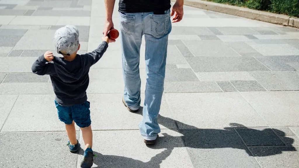 Padre camina de la mano con su pequeño hijo.