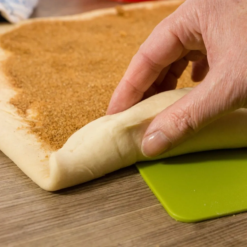 Una persona enrollando los rollitos de canela antes de hornearlos