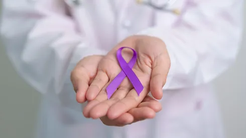 Médico sosteniendo un lazo morado, el color de la concientización de lupus.