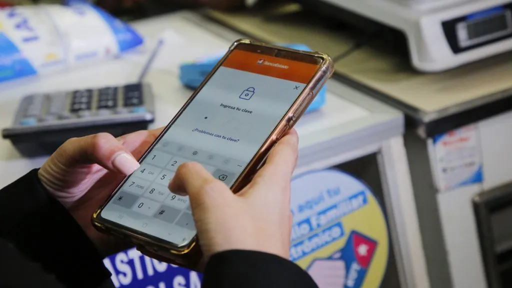 Una mujer abre la app de Banco Estado en su teléfono para pagar una compra en un almacén con el Bolsillo Familiar Electrónico.