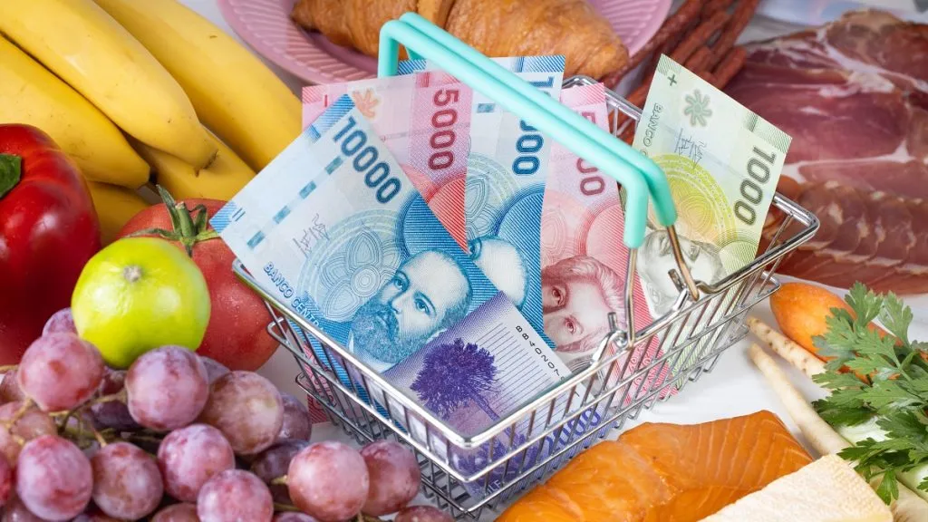 Una canasta miniatura con dinero, sobre frutas y verduras.