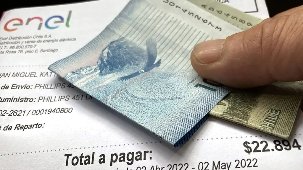 Una mano sostiene una cuenta de la luz junto con unos billetes de $10.000 y $1.000.