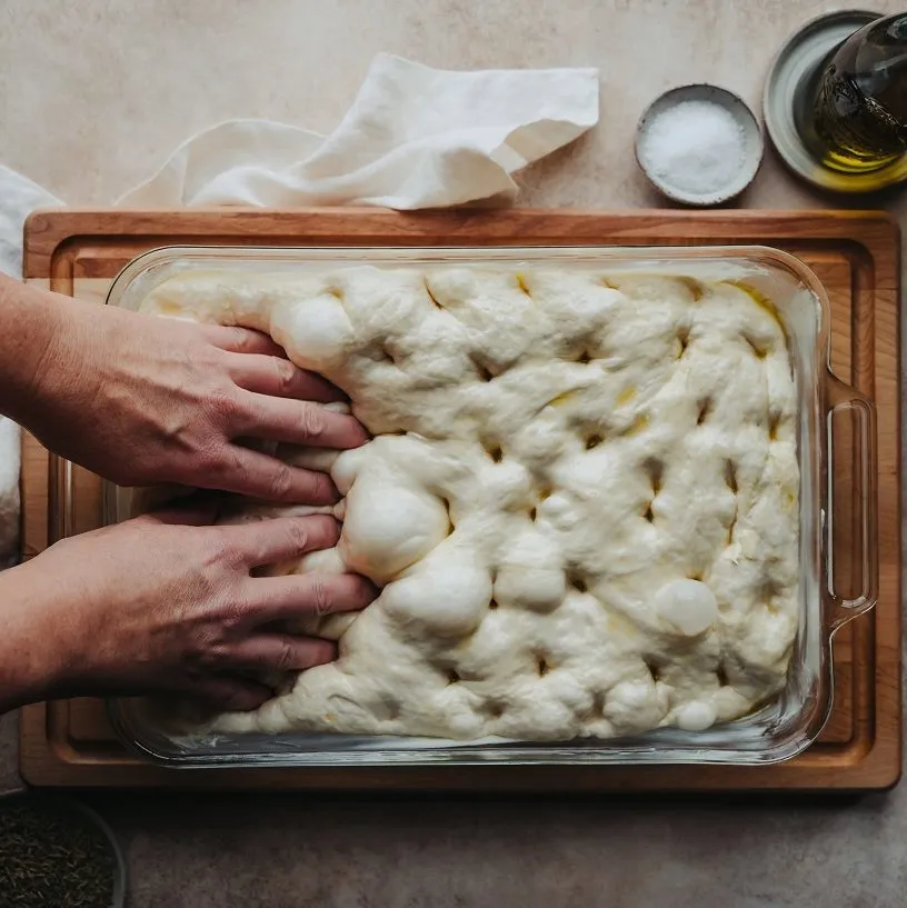 Se ve a unas manos amasando la focaccia en su última etapa, en un molde con aceite de oliva.