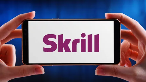 2C982EF POZNAN, POL – MAY 21, 2020: Hands holding smartphone displaying logo of Skrill (formerly Moneybookers), an e-commerce business that allows payments an