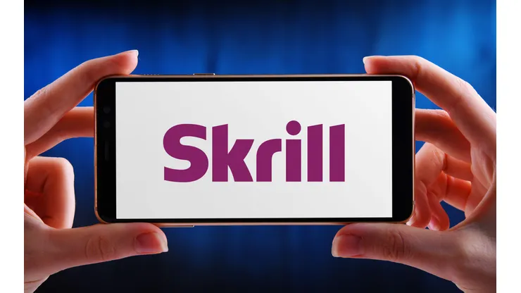 2C982EF POZNAN, POL - MAY 21, 2020: Hands holding smartphone displaying logo of Skrill (formerly Moneybookers), an e-commerce business that allows payments an